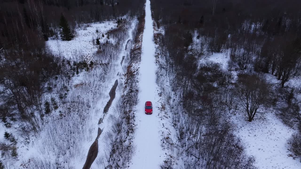 Drone tracks red car from front over snow-covered Latvian backroad forest