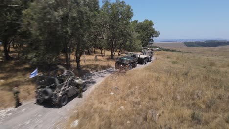 israel army squad soldiers with their vehicles standing in queue at training ground country road, aerial tracking shot