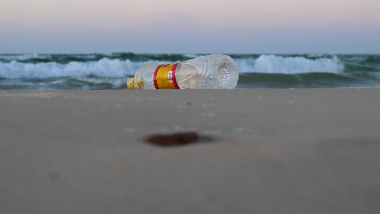 Discarded Plastic Bottle Polluting the Beach with Ocean Waves in the Distance
