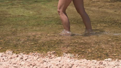 young woman in casual summer clothes walking through a clear river under the sun