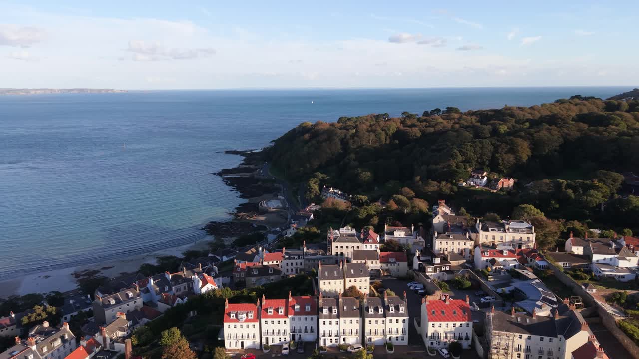High panning footage of St Peter Port Guernsey out to sea from town Val de Terres,clear waters of Havelet Bay harbour Castle Cornet Herm Sark and Jethou in the distance in golden hour on calm day