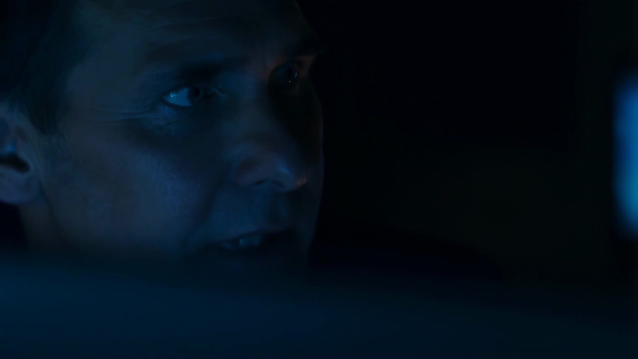 Adult male upper face in extreme closeup shifts gaze from downward inspection to sideways monitoring in low key blue light, with subtle eye rotation, slight head turn, narrowed eyelids over blurred
