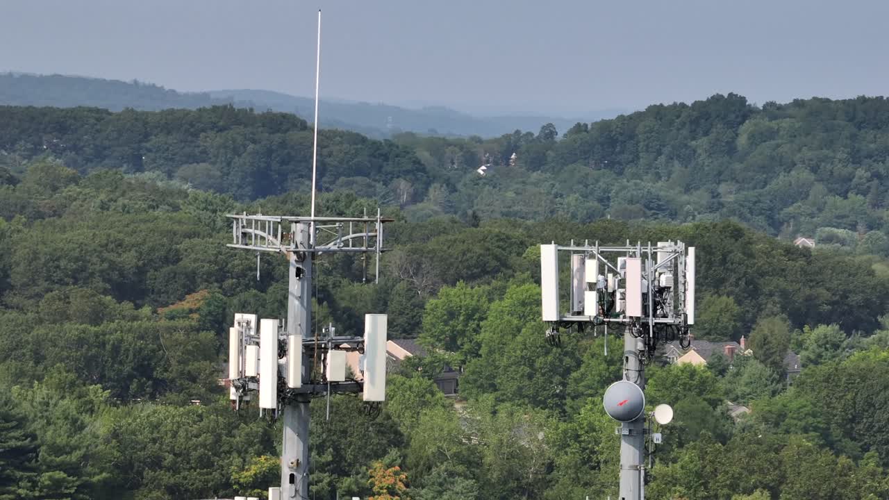 Two Telecommunication transmission tower in rural suburb area of American Town. Housing area between green trees background. Aerial view