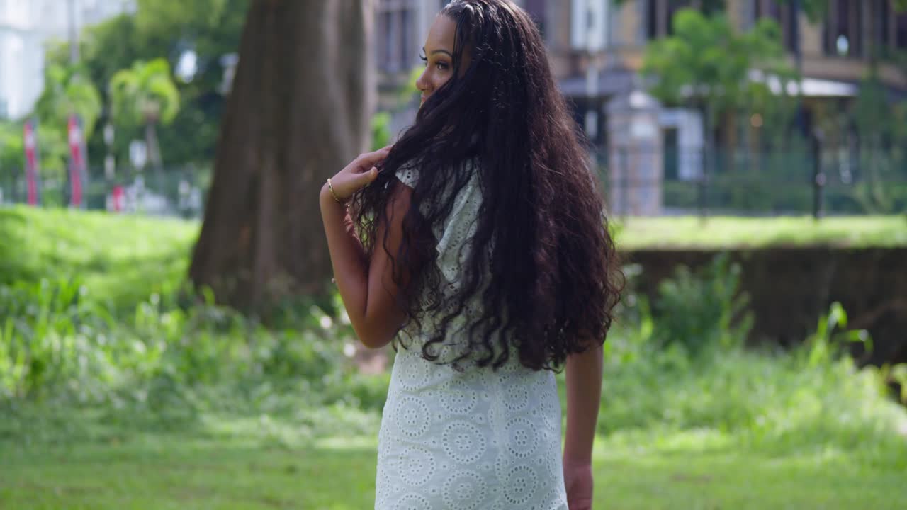 joven de pelo largo y natural caminando por el parque antes de darse la vuelta para revelar una cara bonita