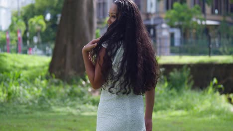 joven de pelo largo y natural caminando por el parque antes de darse la vuelta para revelar una cara bonita