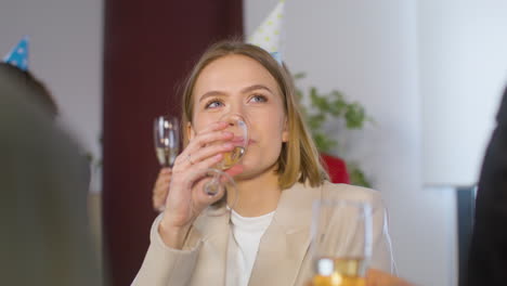 Retrato-De-Una-Mujer-Rubia-Feliz-Con-Sombrero-De-Fiesta-Bebiendo-Champán-Y-Riéndose-Con-Colegas-En-La-Fiesta-De-La-Oficina