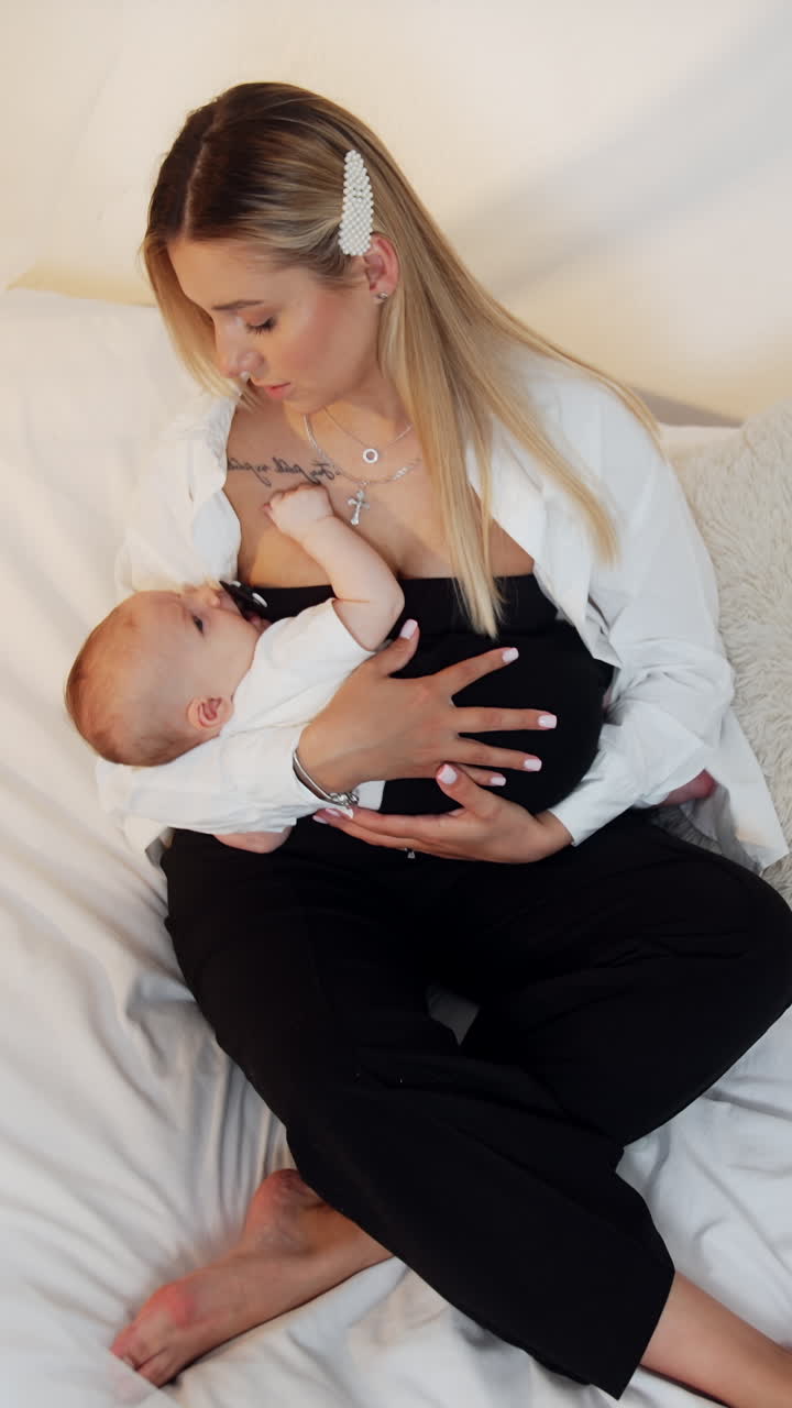 Mother with newborn child sits on the canopy bed with. Caring mom dandling her child. Top view. Vertical video