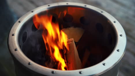 Luxury-polished-metal-barrel-with-logs,-fire-and-sparks-on-wooden-porch