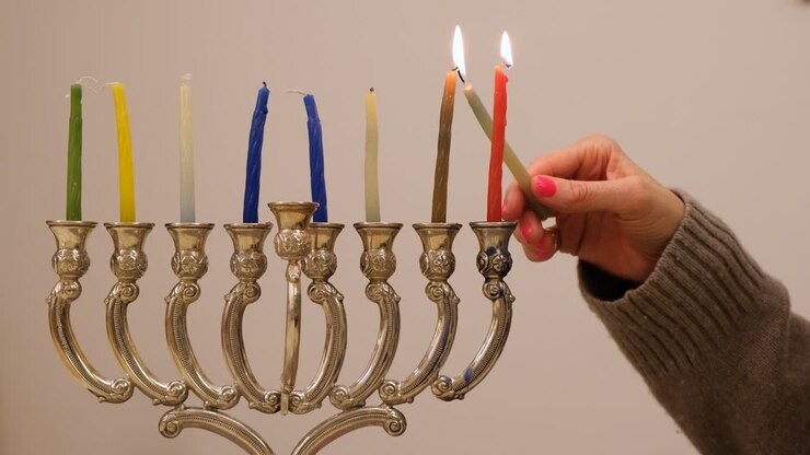 A woman's hand lighting candles in the menorah for Hanukkah