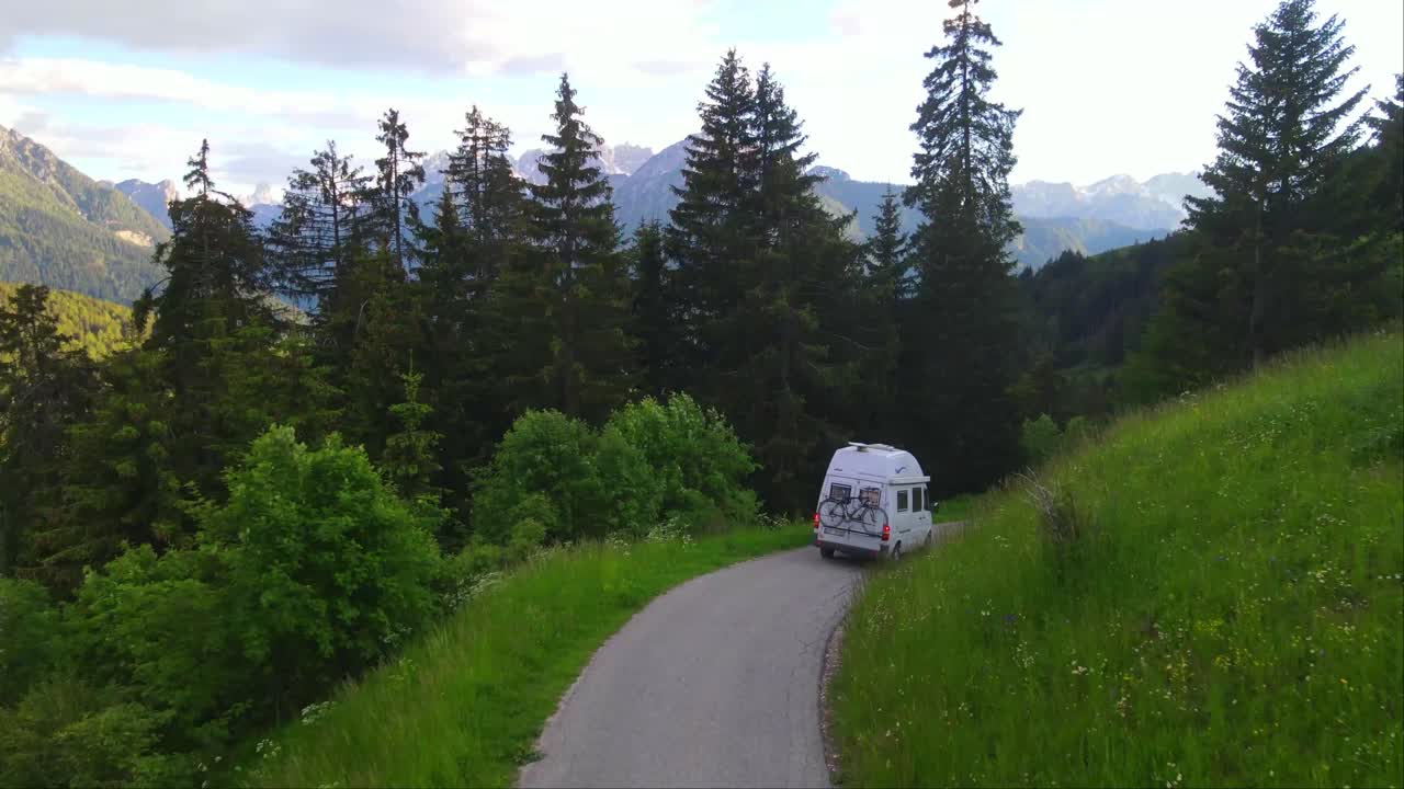 Drone follows a white Camper van through a winding mountain road around the alps in Toblach