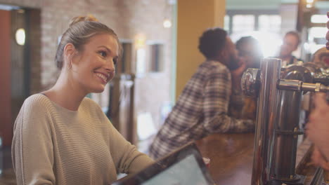 female customer in bar makes socially distanced contactless payment for drinks in health pandemic