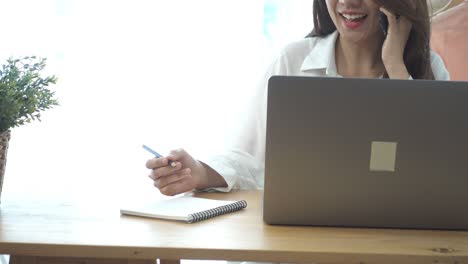 hermosa joven asiática sonriente trabajando en una computadora portátil mientras está sentada en una sala de estar en casa. mujer de negocios asiática usando el teléfono para trabajar en su oficina en casa. disfrutando del tiempo en casa.