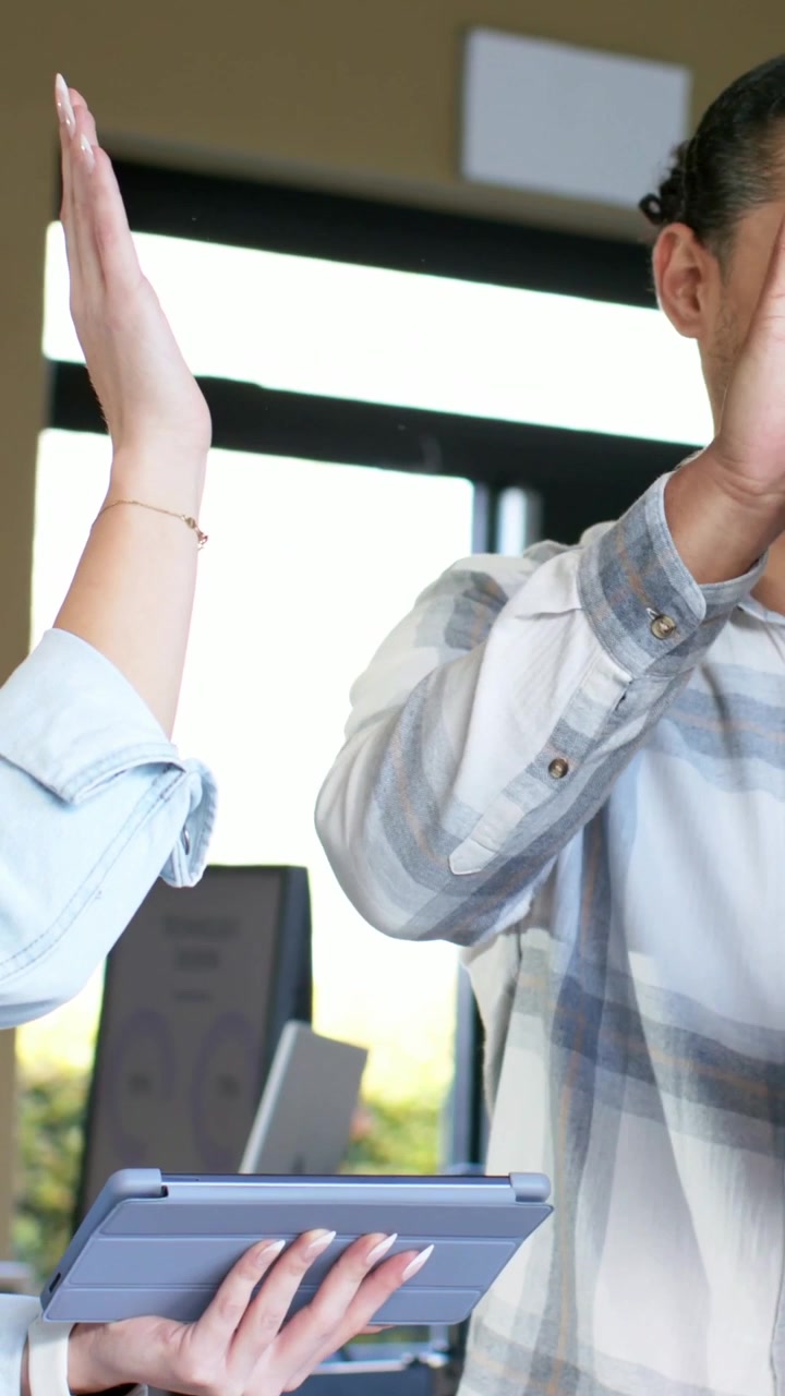 Vertical video: Seeing tablet, man in plaid celebrating by high-fiving colleagues at office, folio
