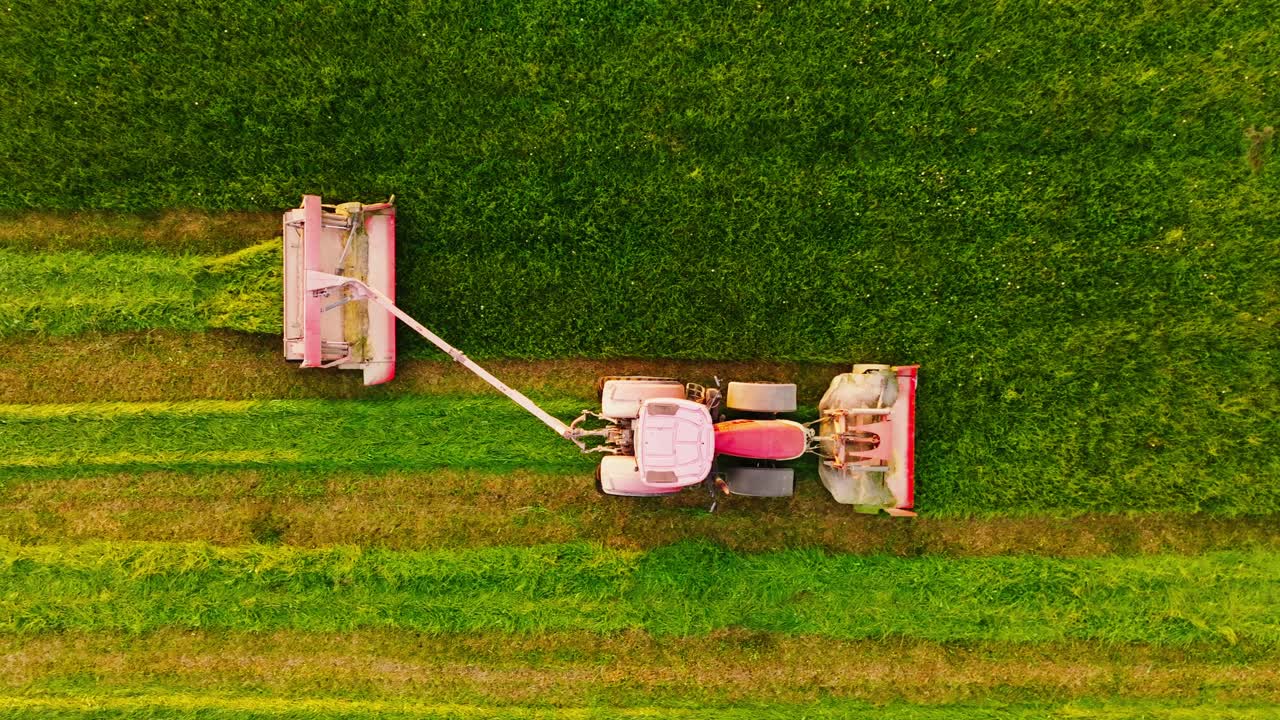 Drone follows tractor mowing grass in rural Latvia during glowing sunset moment