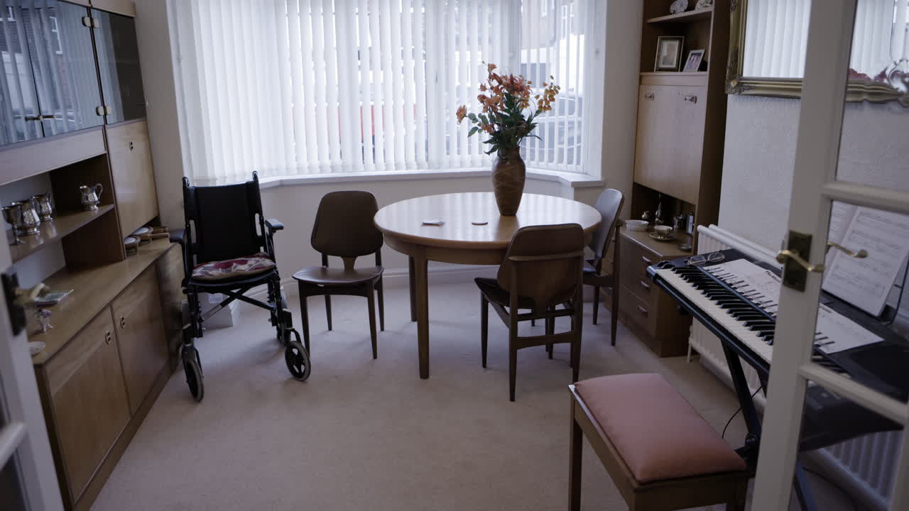A dining room with a wheelchair, table, piano and cabinets