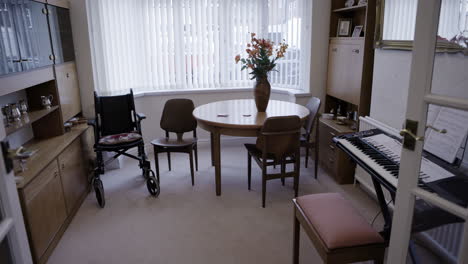 a dining room with a wheelchair, table, piano and cabinets