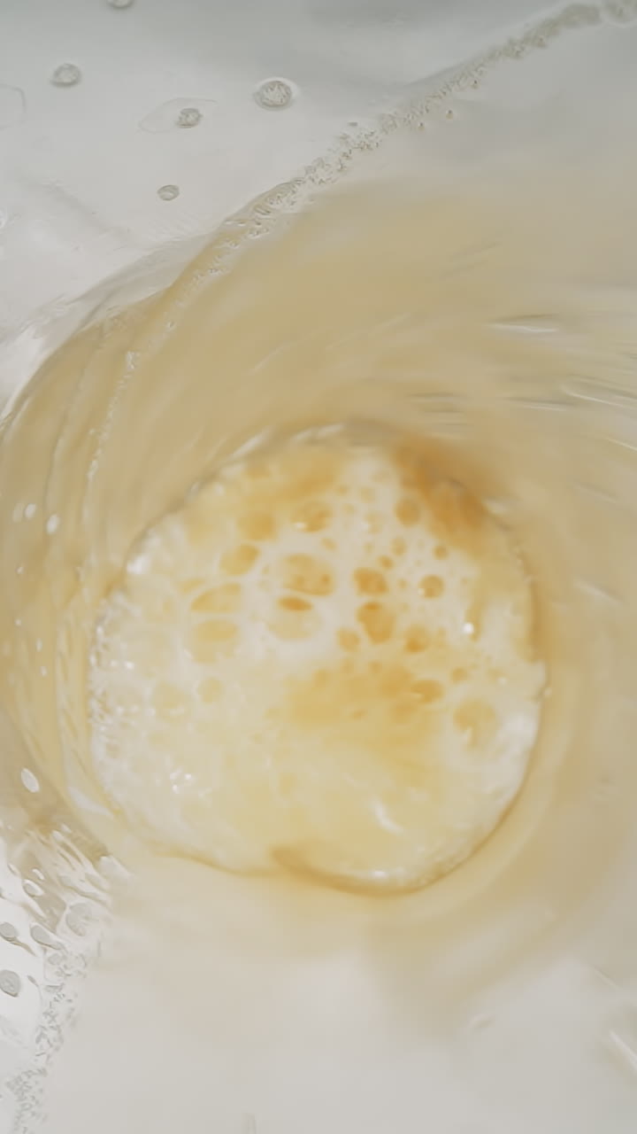 Natural golden beer with heavy froth poured into glass mug macro upper view. Flow of craft alcohol beverage with white fluffy foam slow motion