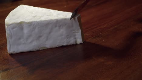 una cuña suave de queso brie es cortada en primer plano en una tabla de madera oscura