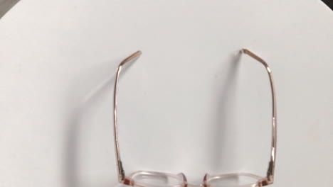 Modern-eyeglasses-in-light-colour-lie-on-a-white-table,-bright-glasses-frame,-slow-motion-footage