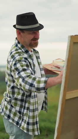 a dedicated sculptor wearing a black hat, checkered shirt, and jeans is intently painting a canvas in a serene grass field. the artist s focus and concentration on the artwork