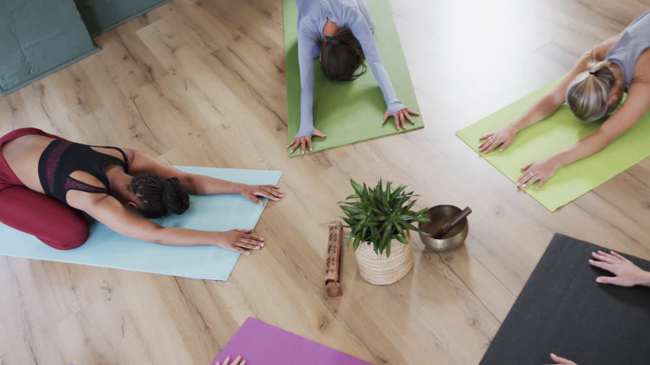 mujeres multirraciales practicando la postura infantil alrededor de la planta y el cuenco de canto en el estudio de yoga