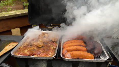 white smoke rising over the aluminum foil tray with marinated meat and sausages - grilling barbecue