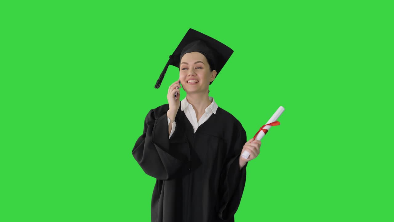 Studentessa felice in toga di laurea che parla emozionata al telefono mentre cammina con il diploma su uno schermo verde, Chroma Key