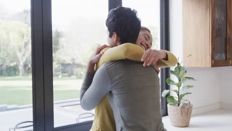 Happy-caucasian-lesbian-couple-embracing-and-smiling-in-sunny-kitchen