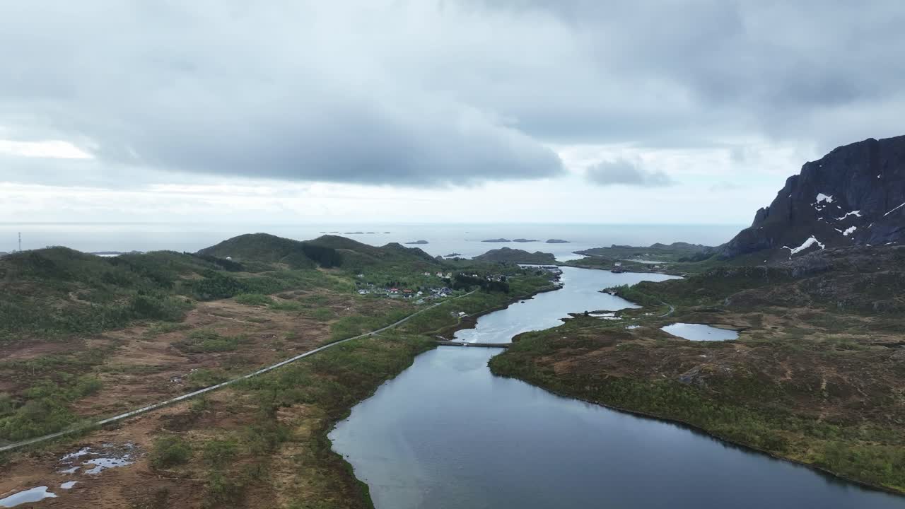 Wide aerial over Hopspollen south of Svolvaer showing bridge, fjord reflections, sea horizon and surrounding mountains on cloudy spring day