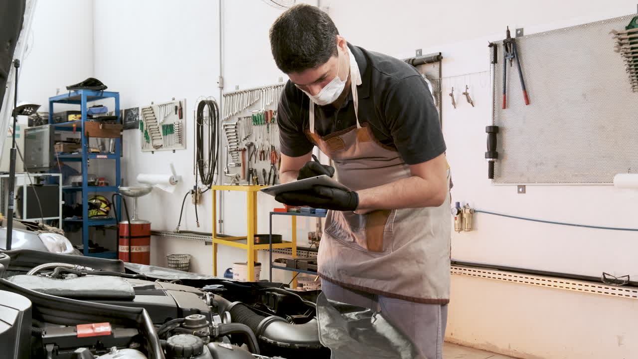 mecánico con máscara covid revisando el auto y tomando notas en el bloc de notas digital