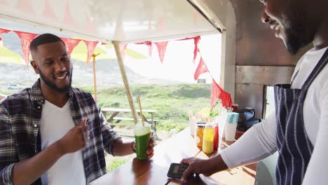 el dueño de un camión de comida afroamericano sonriente toma el pago de la tarjeta de crédito del hombre y la mujer que sirve