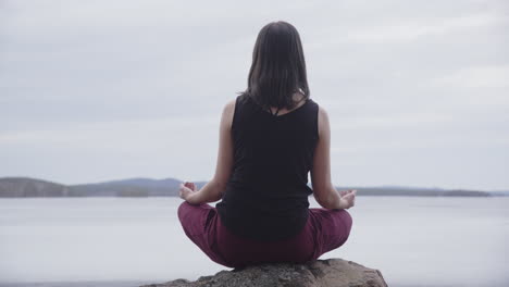 Frau-In-Padmasana-Position-Auf-Einem-Felsen-Meditiert-Mit-Blick-Auf-Den-See