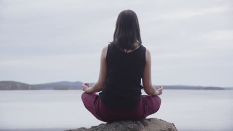 mujer en posición de padmasana en la roca meditando con vistas al lago