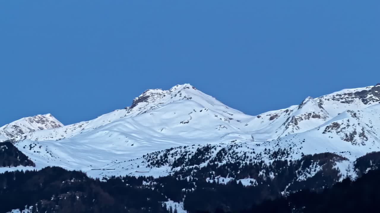 Paesaggio invernale mozzafiato con maestose catene montuose coperte di neve e scure foreste sempreverdi a Nauders, Austria, contro un orizzonte azzurro brillante.