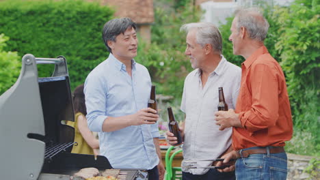 Three-Senior-Male-Friends-Cooking-Outdoor-Barbeque-And-Drinking-Beer-At-Home-Together