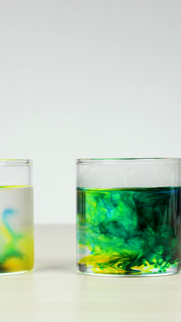 Coloranti alimentari giallo e blu vivaci che si mescolano in bicchieri d'acqua.