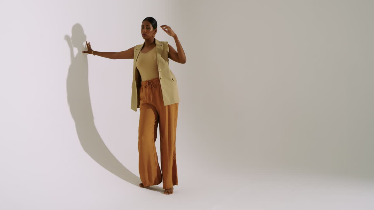 Entering frame Indian woman walking toward studio wall tracing shadow and modeling, copy space