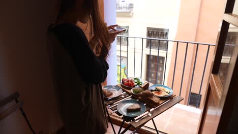 woman taking photo of breakfast on balcony