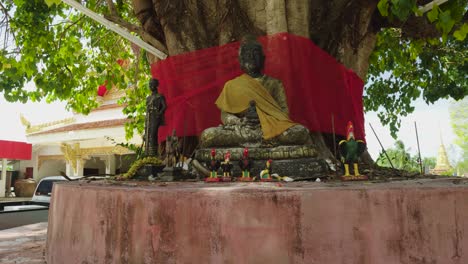 bodhi-baum mit sitzenden buddha- und hahnstatuen im thailändischen tempel