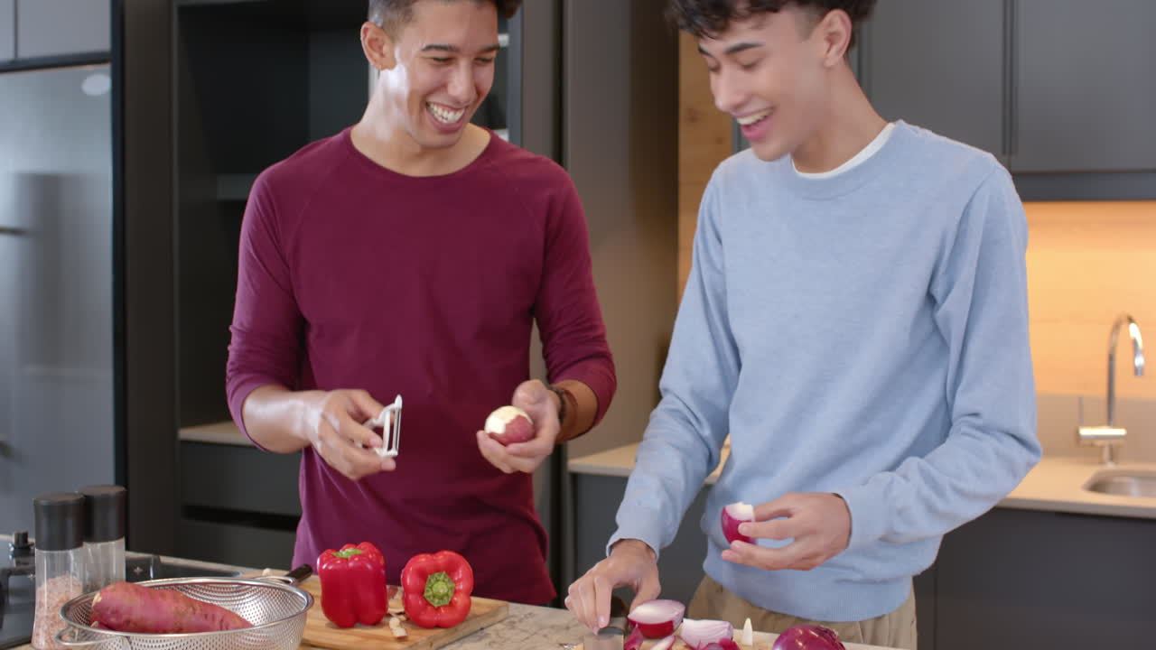 Cooking , multiracial gay couple peeling vegetables and smiling in modern kitchen, at home