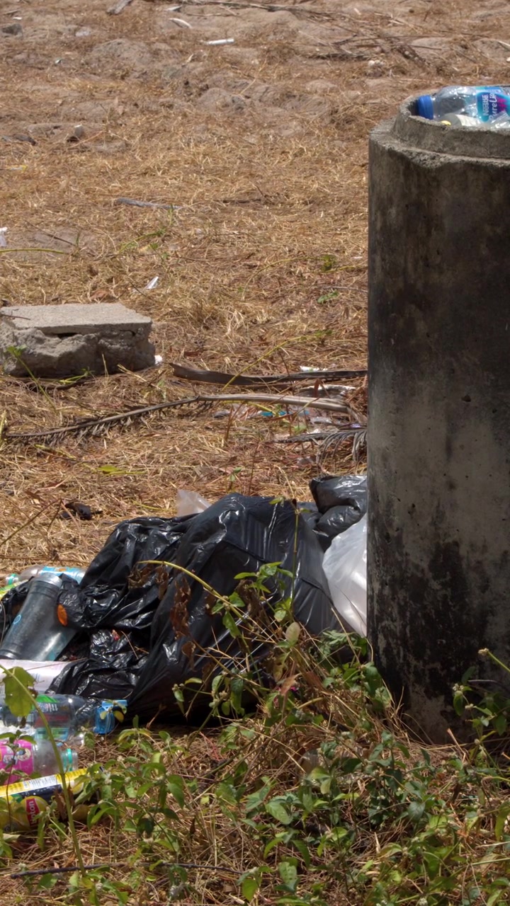 Inquadratura media statica di bottiglie di plastica e sacchi neri della spazzatura che sporcano un campo erboso secco.