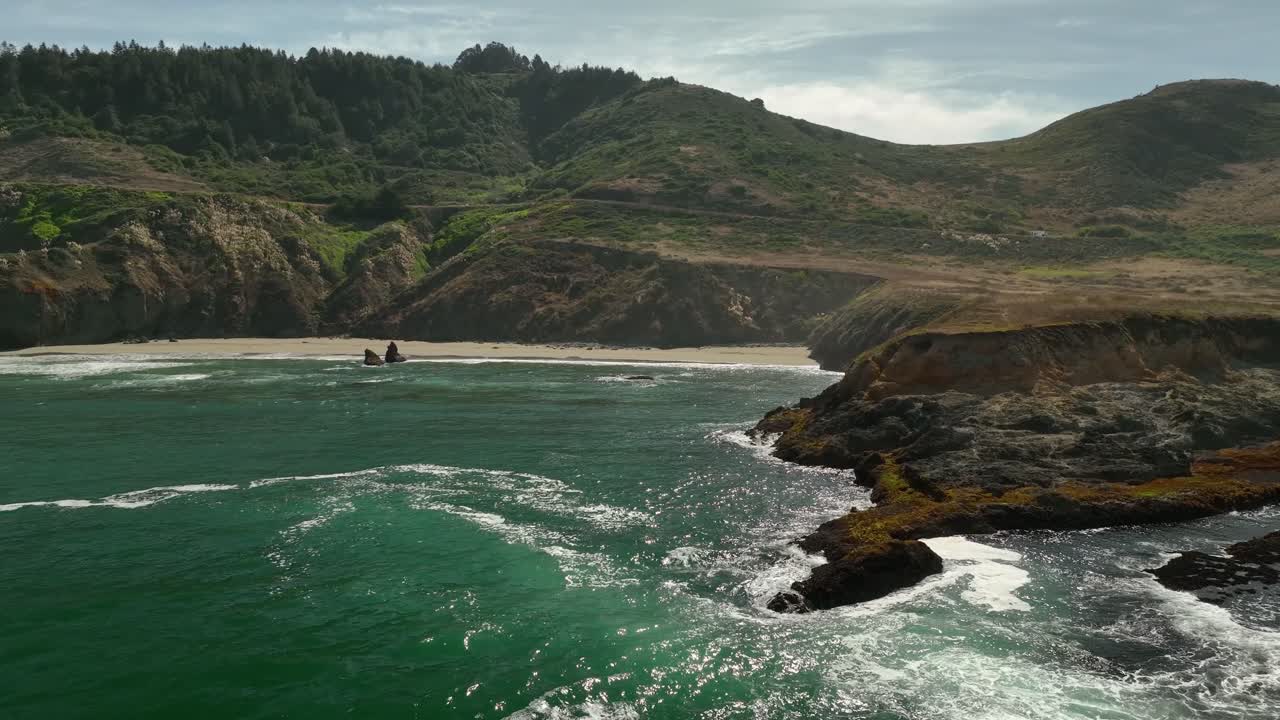 정오에 캘리포니아의 반짝이는 해안선 위로 우뚝 솟은 로밍 푸른 언덕의 드론 샷