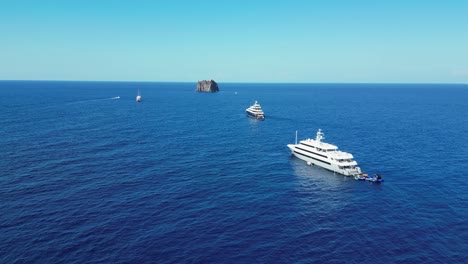 Boats-and-Strombolicchio-Volcano-Island-at-Stromboli,-Aeolian-Islands,-Sicily,-Italy---Aerial-4k-Circling