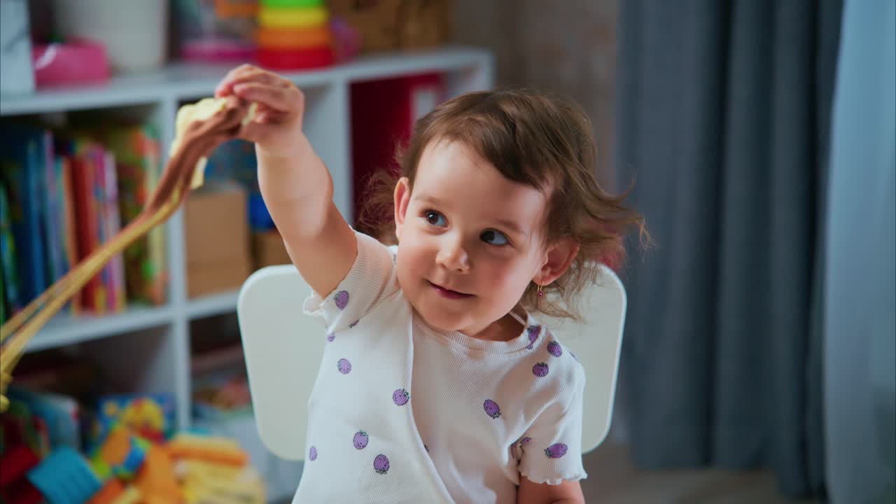 Young Child Enjoys Stretching and Playing with Colorful Slime in a Bright, Engaging Room Full of Toys and Books