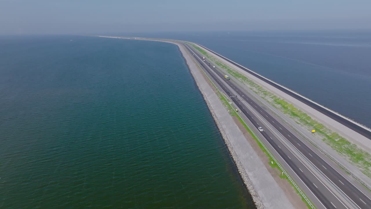 Drone zoom in approaching the Afsluitdijk highway dividing the North Sea and IJsselmeer under clear daylight