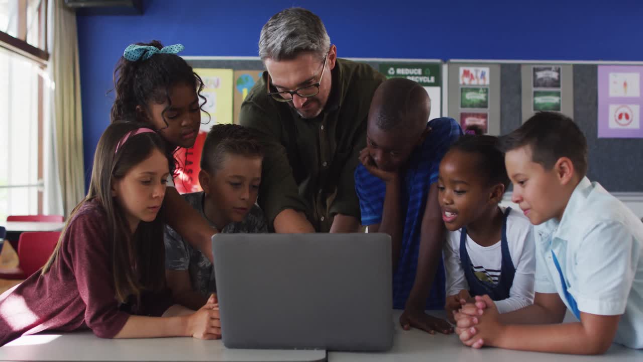 Diverse male teacher and group of schoolchildren looking at laptop