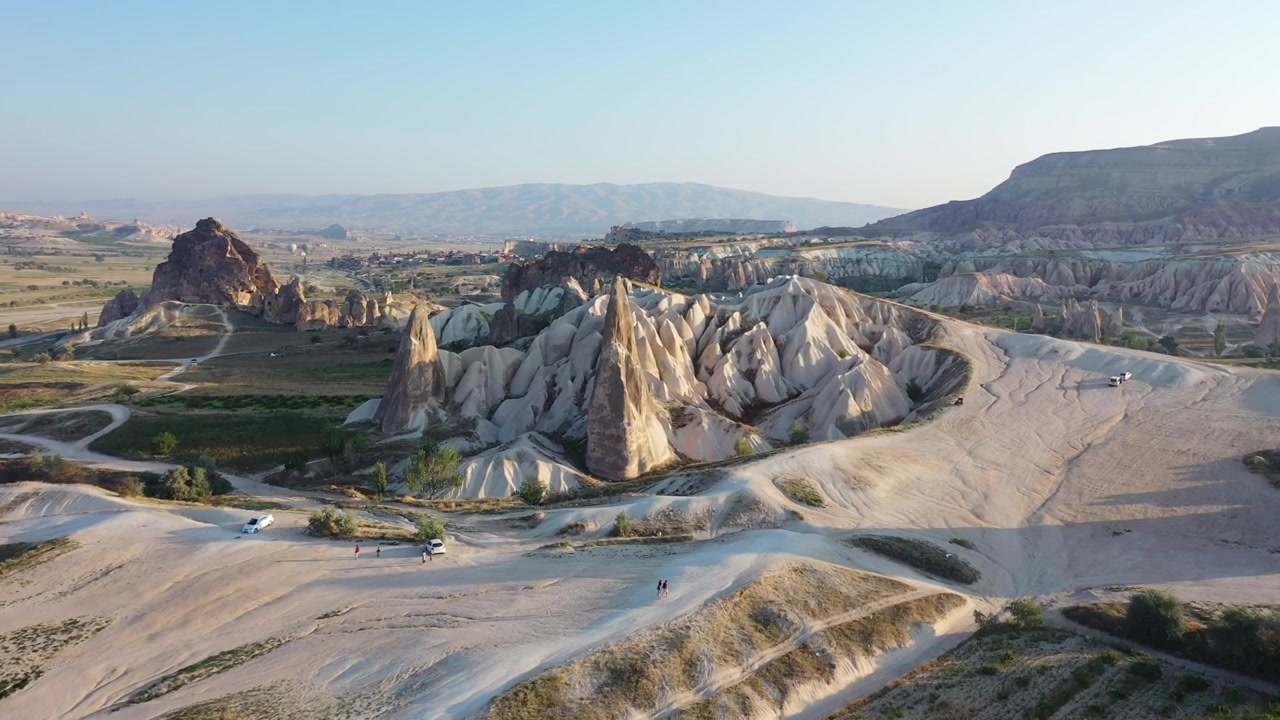 Ampia ripresa aerea con drone di una mongolfiera che fluttua oltre imponenti formazioni rocciose a camino di fata sopra il paesaggio panoramico della valle della Cappadocia, Nevsehir, Turchia nella morbida luce del mattino