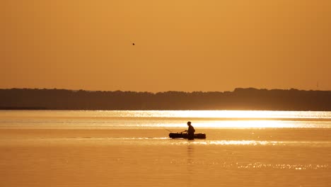 fisherman in a boat at golden sunset time. silhouette of man floating with oars on a small rowboat in the evening. beautiful sunset in the river and man in boat with fishing rods.