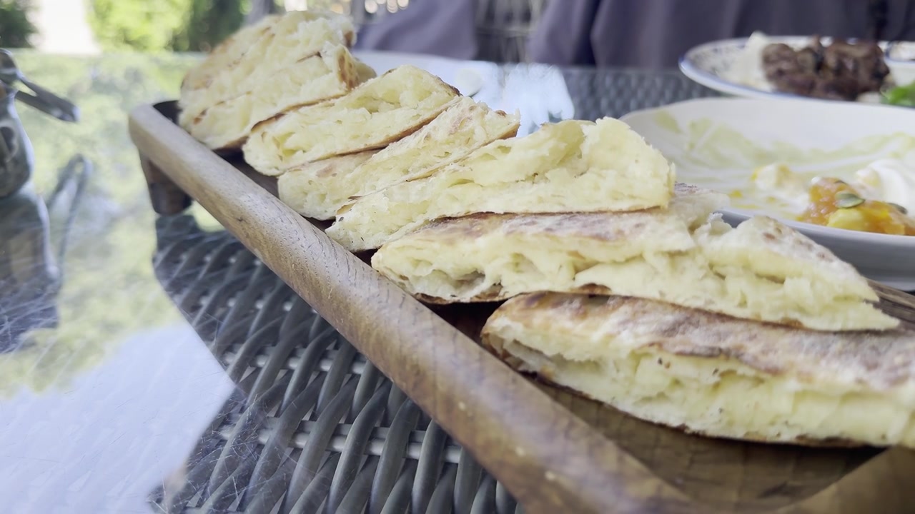 A close-up shot of sliced Dagestani chudu, a traditional savory flatbread, served on a wooden tray at an outdoor restaurant in Izberbash, Republic of Dagestan, Russia