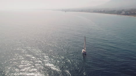 yacht sailing along the coastline of spain, drone moving backwards and tilting into the horizon